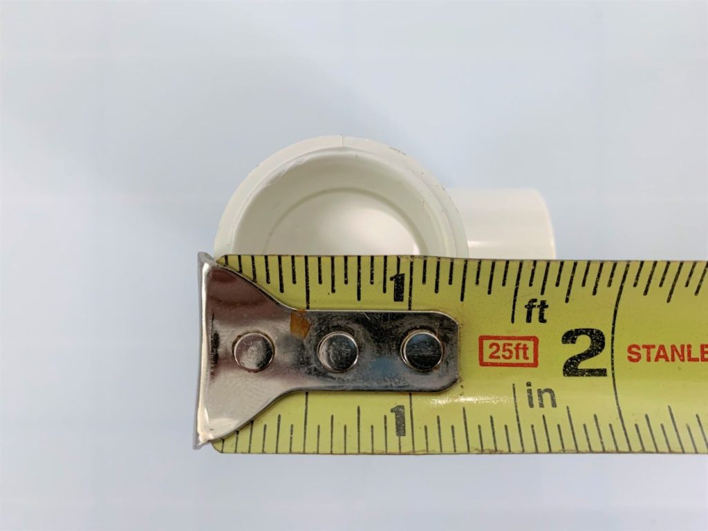 A tape measure measuring the diameter of a PVC elbow joint