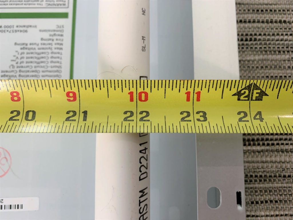 A yellow tape measure measuring 22.25" with a PVC pipe and metal rim in the background
