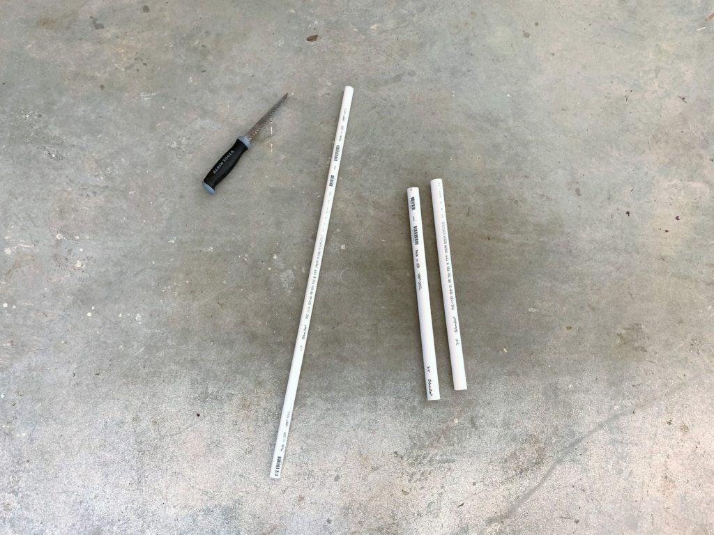 A length of 1/2" PVC pipe, two sections of 3/4" PVC pipe, and a handsaw laying on the ground