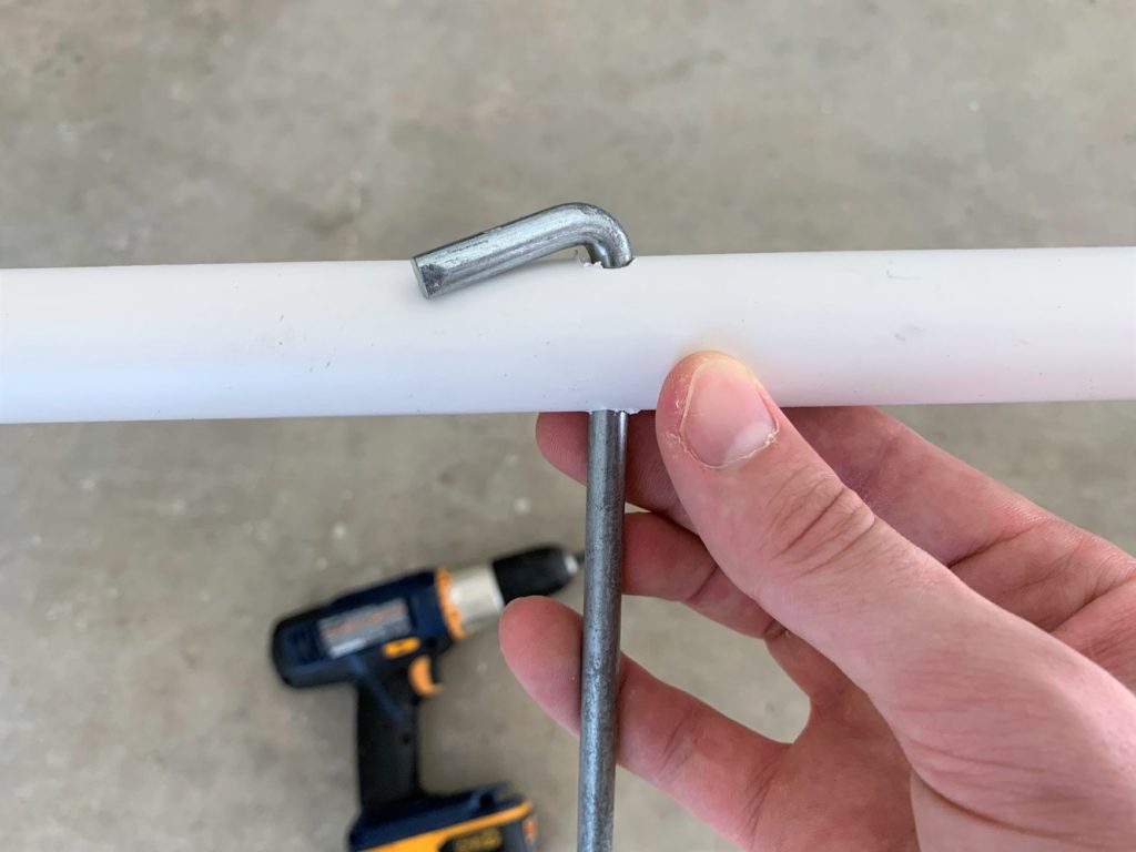 A hand holding a piece of PVC pipe with a metal tent stake stuck through in a hole in the pipe