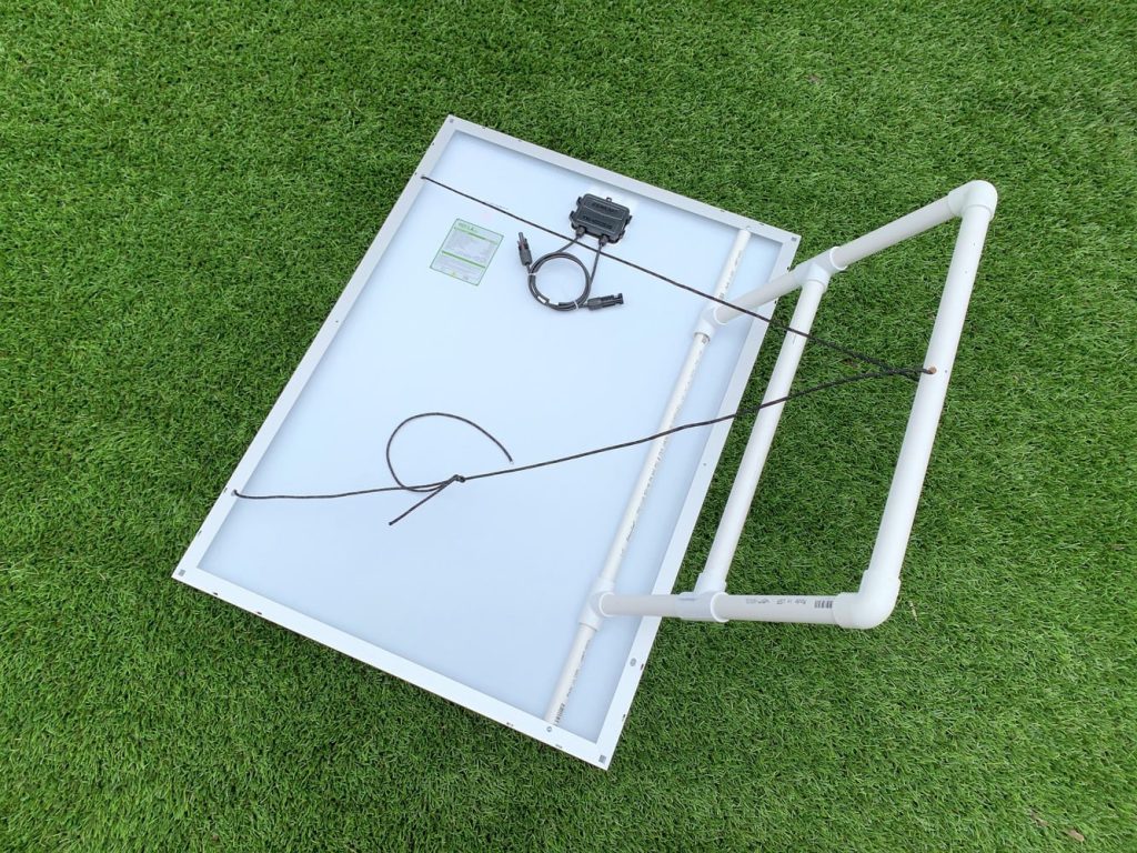 A solar panel with a portable solar panel mount laying upside down on astroturf