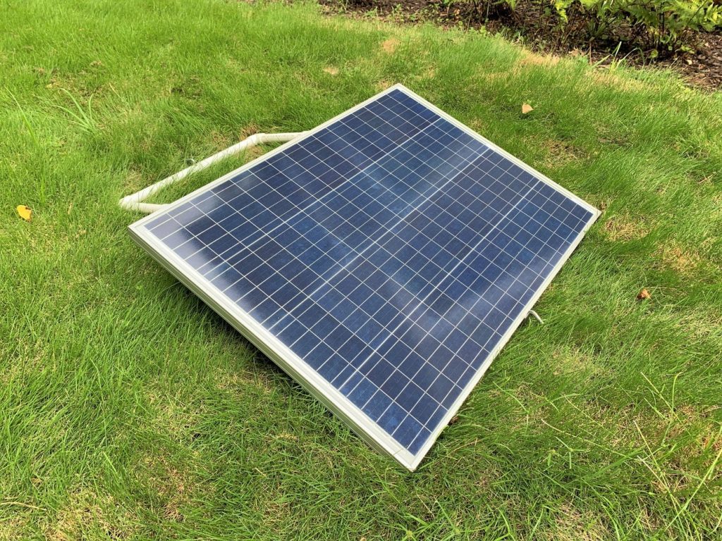 The sun shining on a blue solar panel tilted at an angle in a yard
