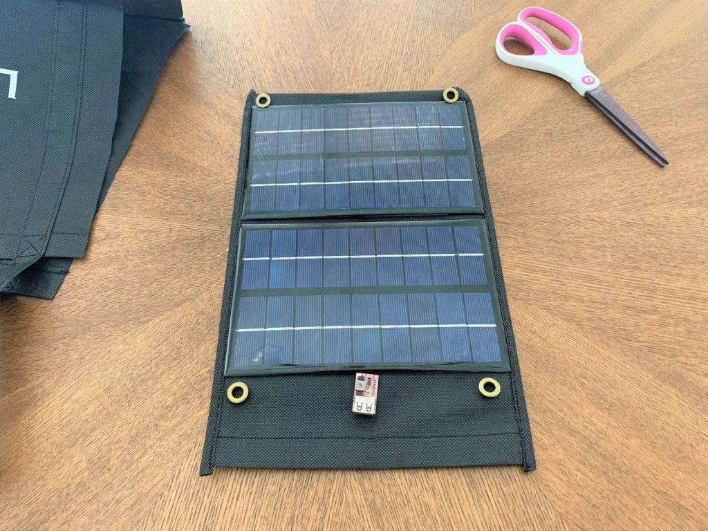 Two 3W 9V solar panels, four eyelets, and a USB buck converter laid on a strip of cut fabric