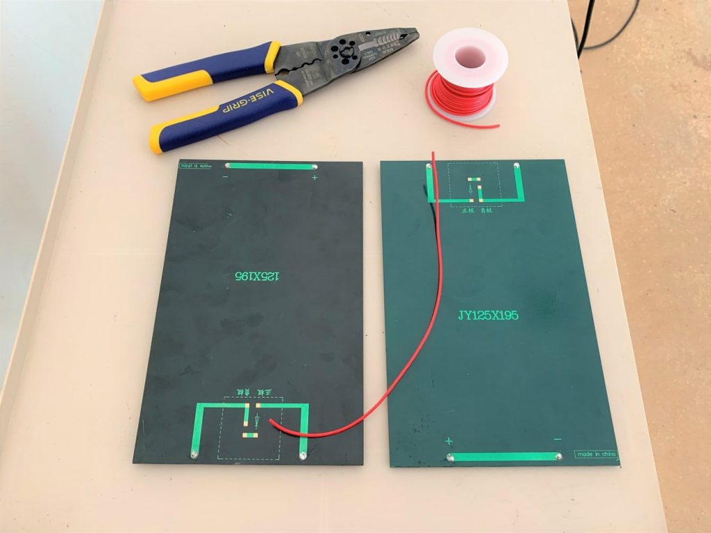 Two 3W 9V solar panels, a length of red wire, a roll of red wire, and wire strippers laid on a surface