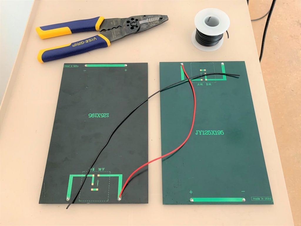 Two small solar panels, a length of black wire, a roll of black wire, and wire strippers laid out on a surface